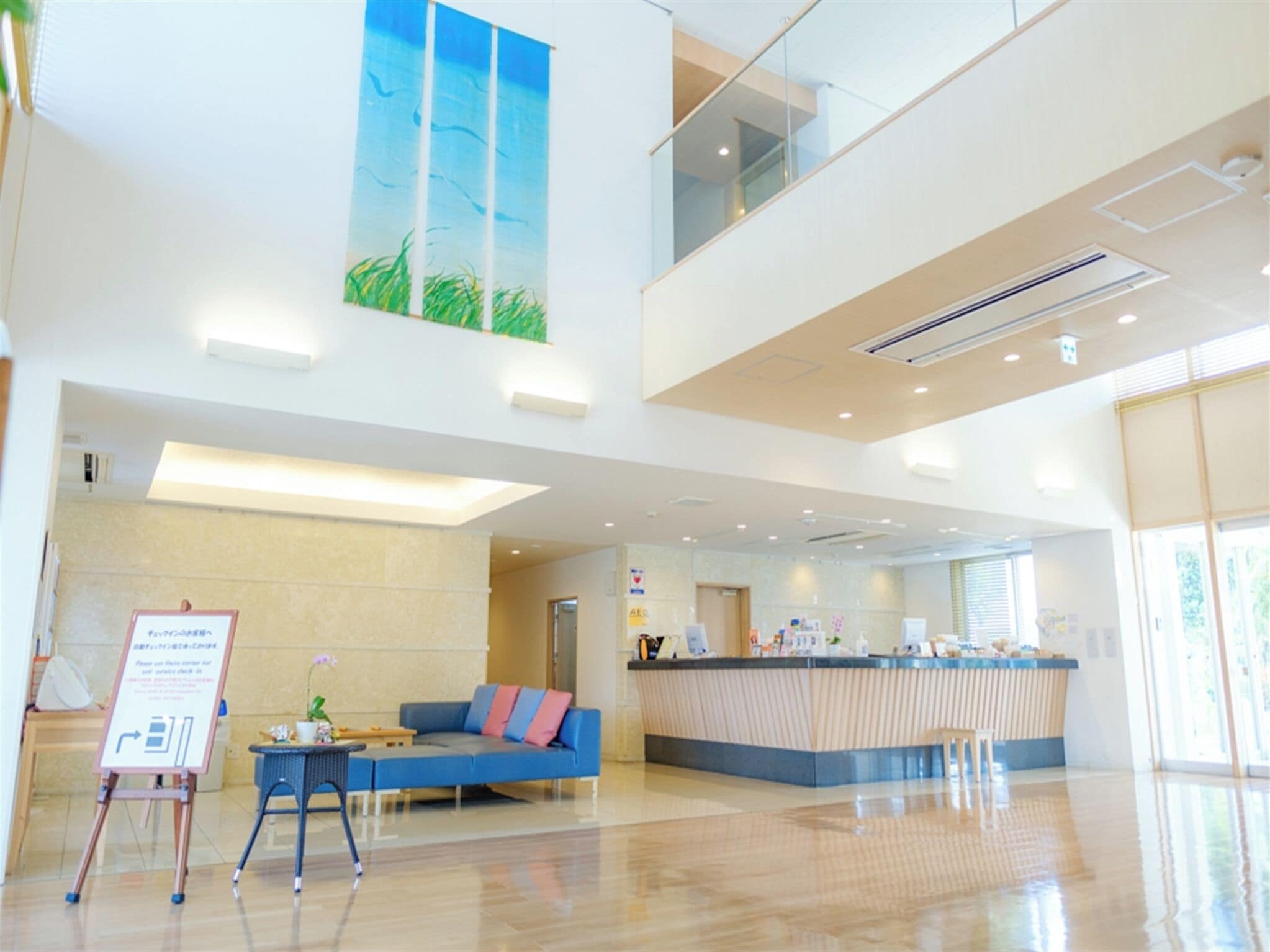A spacious lobby with a reception desk, a blue sofa, and a large painting of a blue sky and grass.