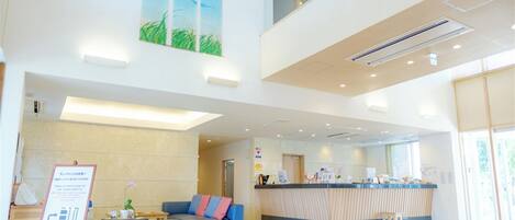 A spacious lobby with a reception desk, a blue sofa, and a large painting of a blue sky and grass.