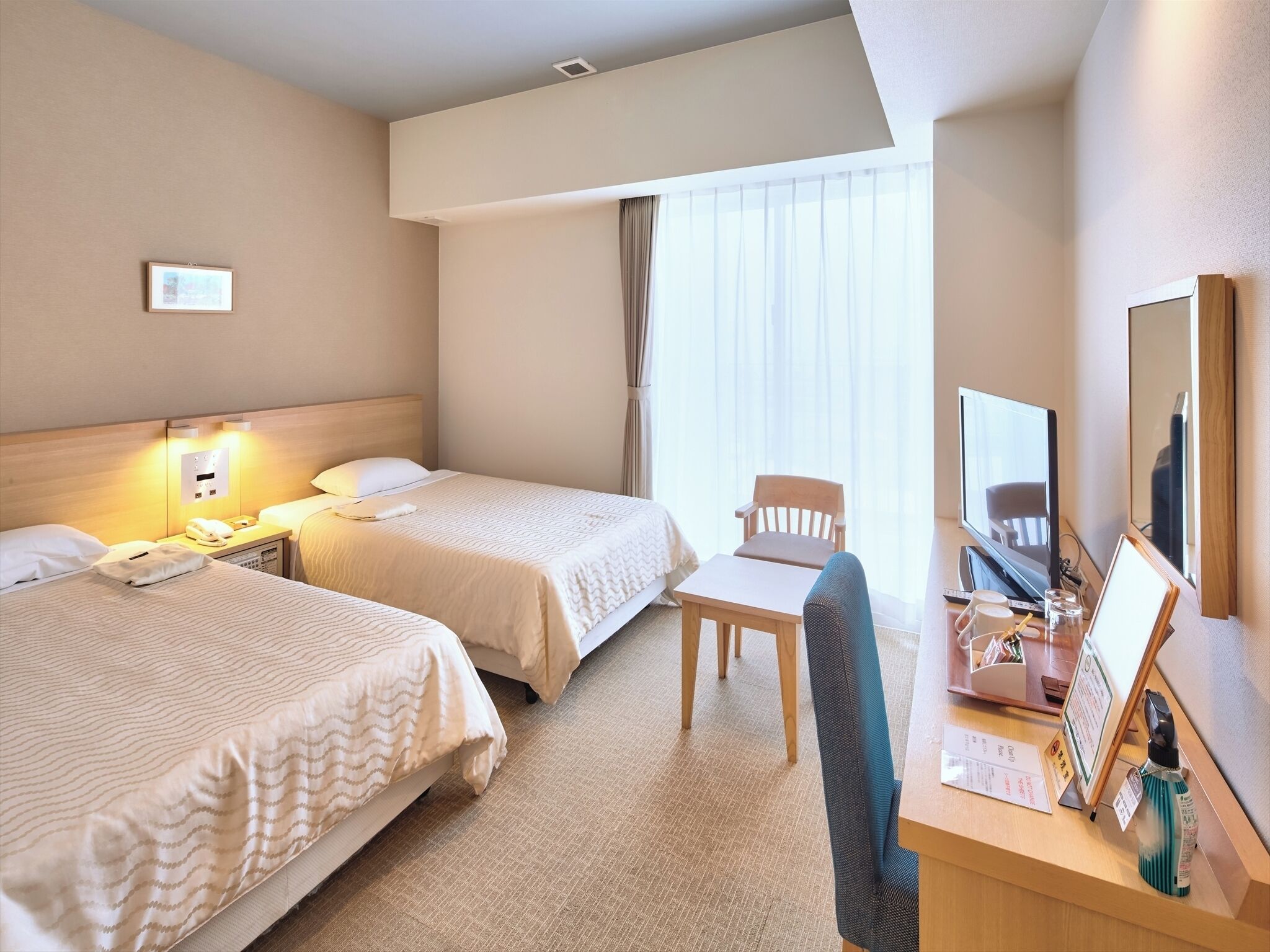 A hotel room with two beds, a desk with a chair, a television, and a mirror.