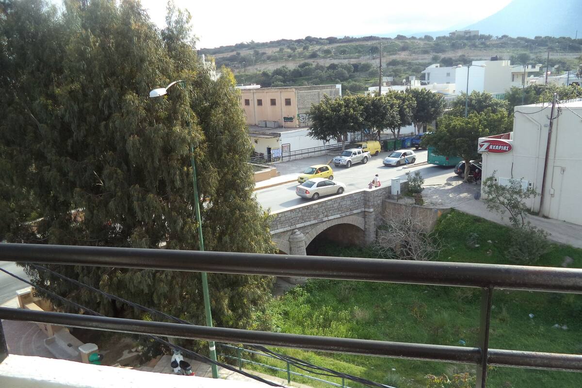 Blick vom Balkon auf eine Straße mit einer Steinbrücke, Fahrzeugen und Gebäuden.
