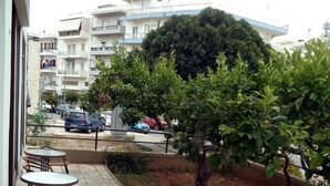 An outdoor seating area with wicker chairs and a tiled floor, overlooking a street with parked cars and a building with balconies. - Hotel Gefyra (Agios Nikolaos)