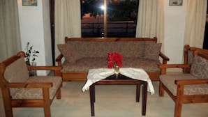 A living room with a sofa, two armchairs, a coffee table with a vase, and curtains. - Hotel Gefyra (Agios Nikolaos)