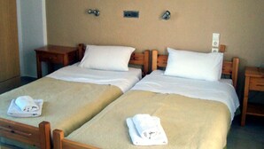 A double room with two single beds, each with a wooden headboard, white linens, and a folded towel on the bed. There are wooden nightstands with lamps, a wall-mounted light switch, and a small shelf with items. - Hotel Gefyra (Agios Nikolaos)
