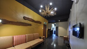 A hotel lobby with a long reception desk, a sofa with striped cushions, a modern chandelier, and a flat-screen TV mounted on the wall. - Le Metrotel (Ipoh)