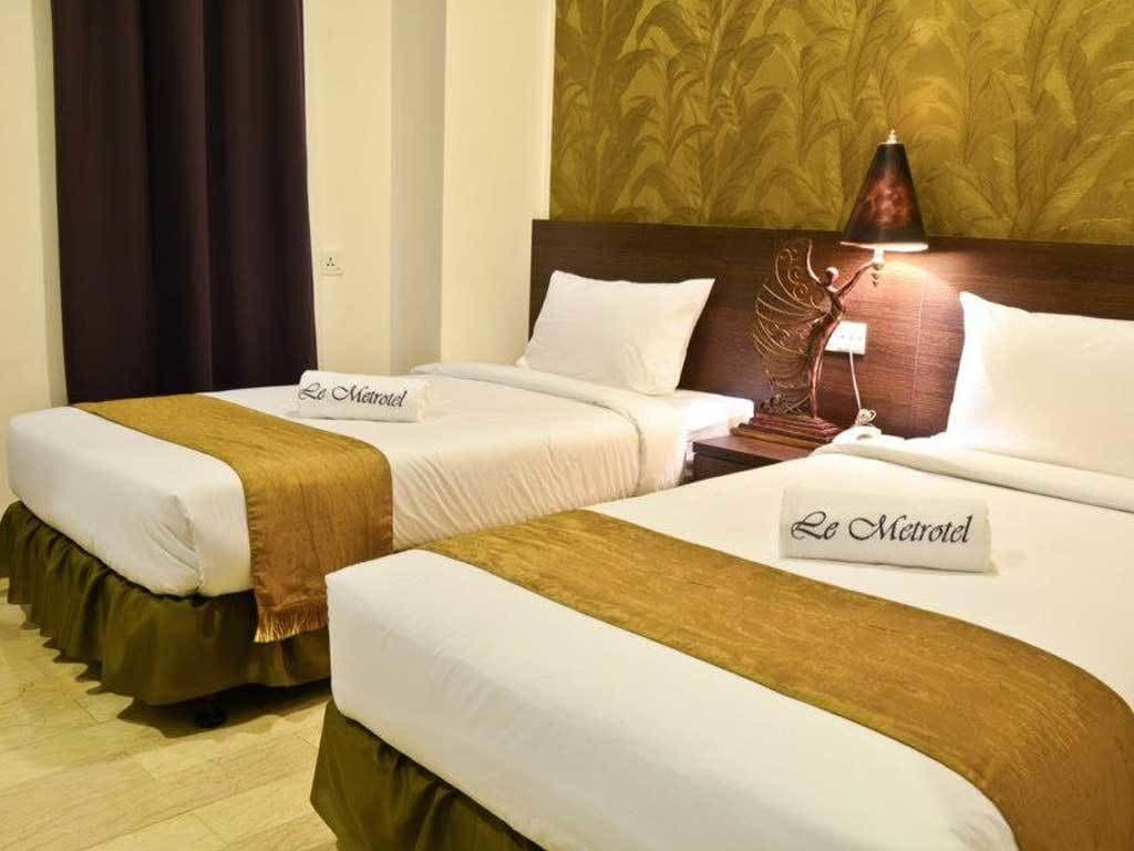 Two identical twin beds in a hotel room with a headboard, a nightstand, a lamp, and a bed runner with the hotel name.
