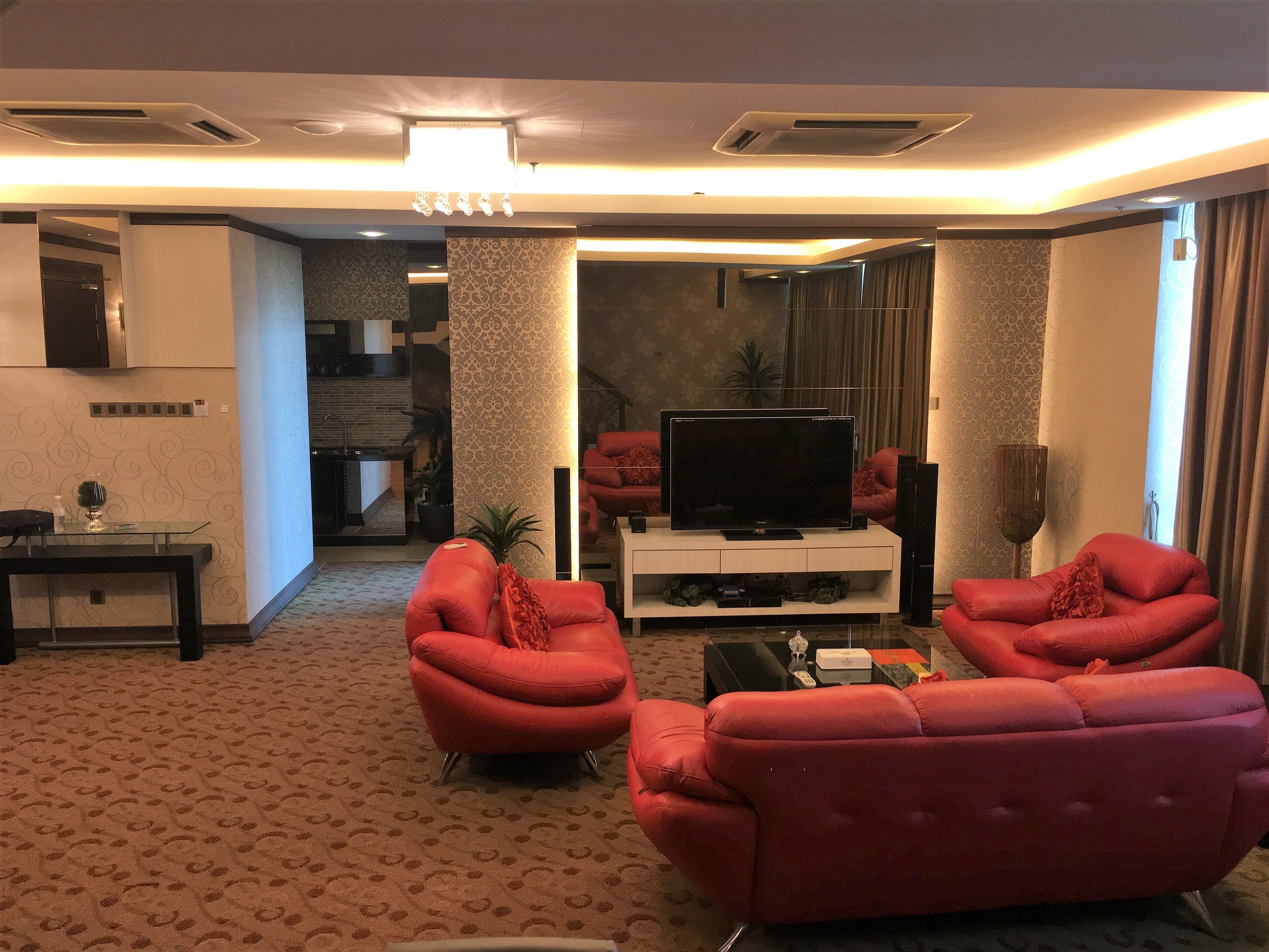 Een moderne woonkamer met een flatscreentelevisie, rode leren banken en een kamerbreed tapijt met een patroon.