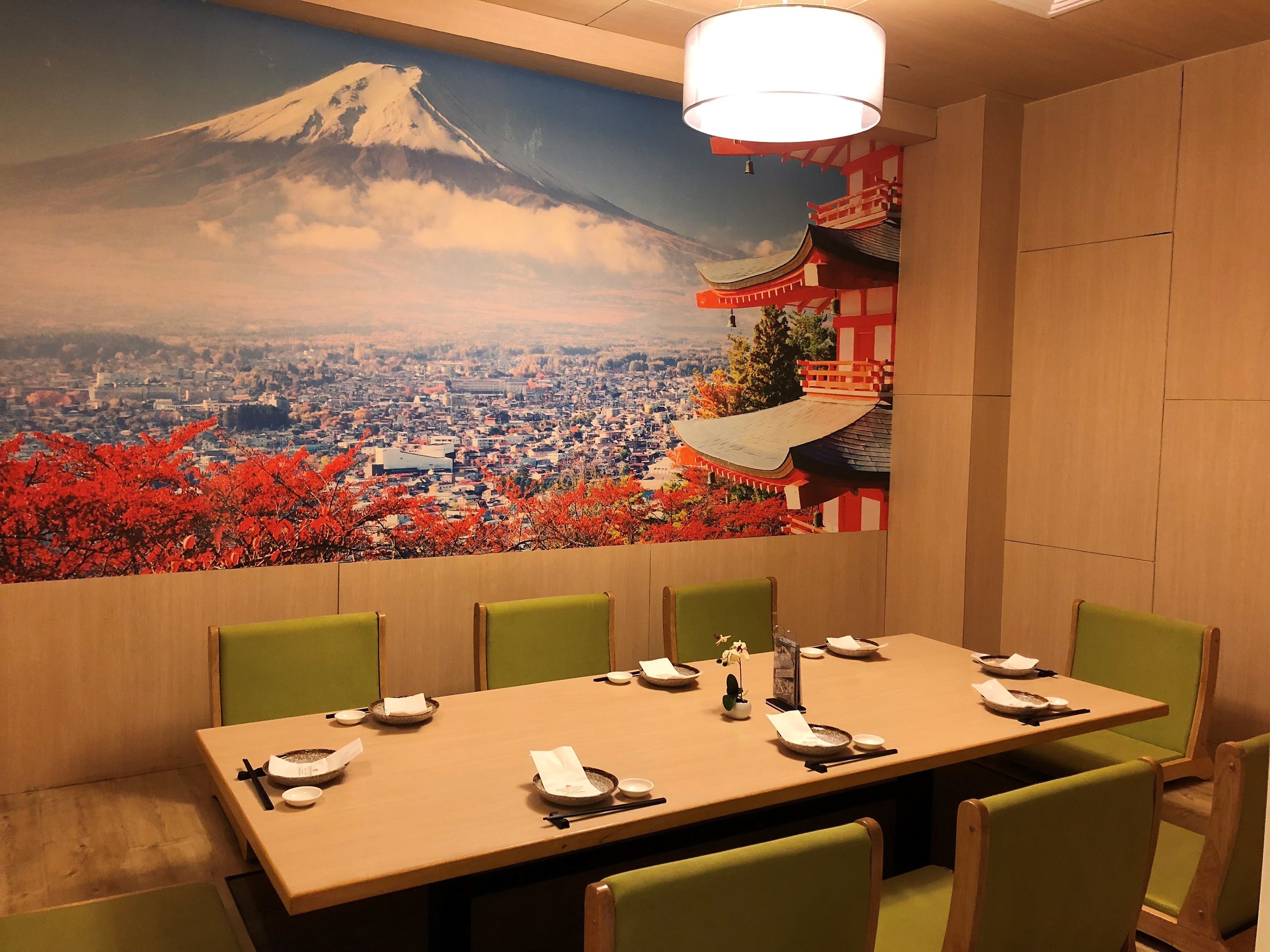 Comedor con una mesa dispuesta para cuatro personas, sillas y un mural que muestra una montaña y un paisaje urbano.