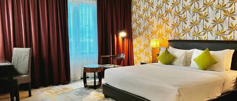 A hotel room with a bed, a desk, a chair, a lamp, and a patterned wall.