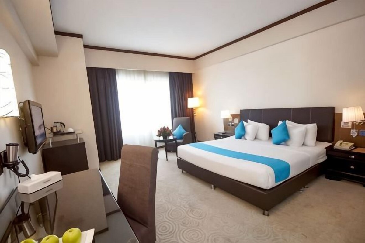 Habitación de hotel con una cama grande, un escritorio, una silla, un televisor y una lámpara de escritorio.
