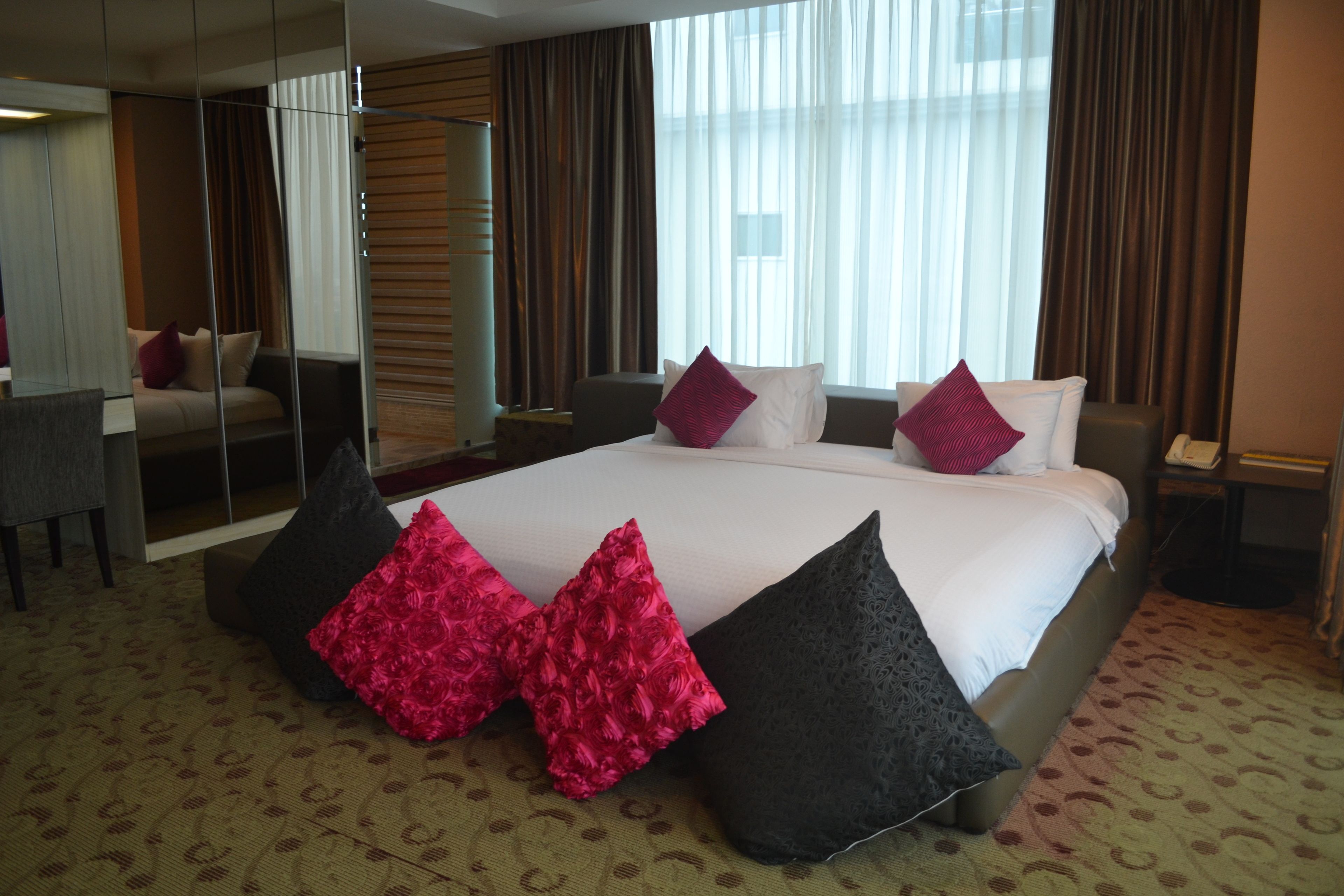 A hotel room with a large bed, two bedside tables, a mirror, and a view of the city through large windows.