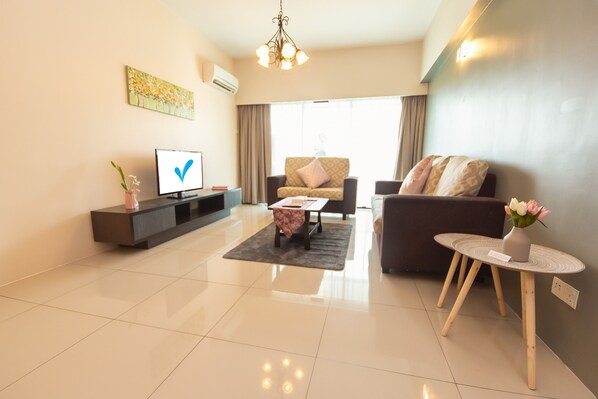 A modern living room with a flat-screen TV, a sofa, a coffee table, and a small side table with a vase. - Kinta Riverfront Hotel & Suites (Ipoh)