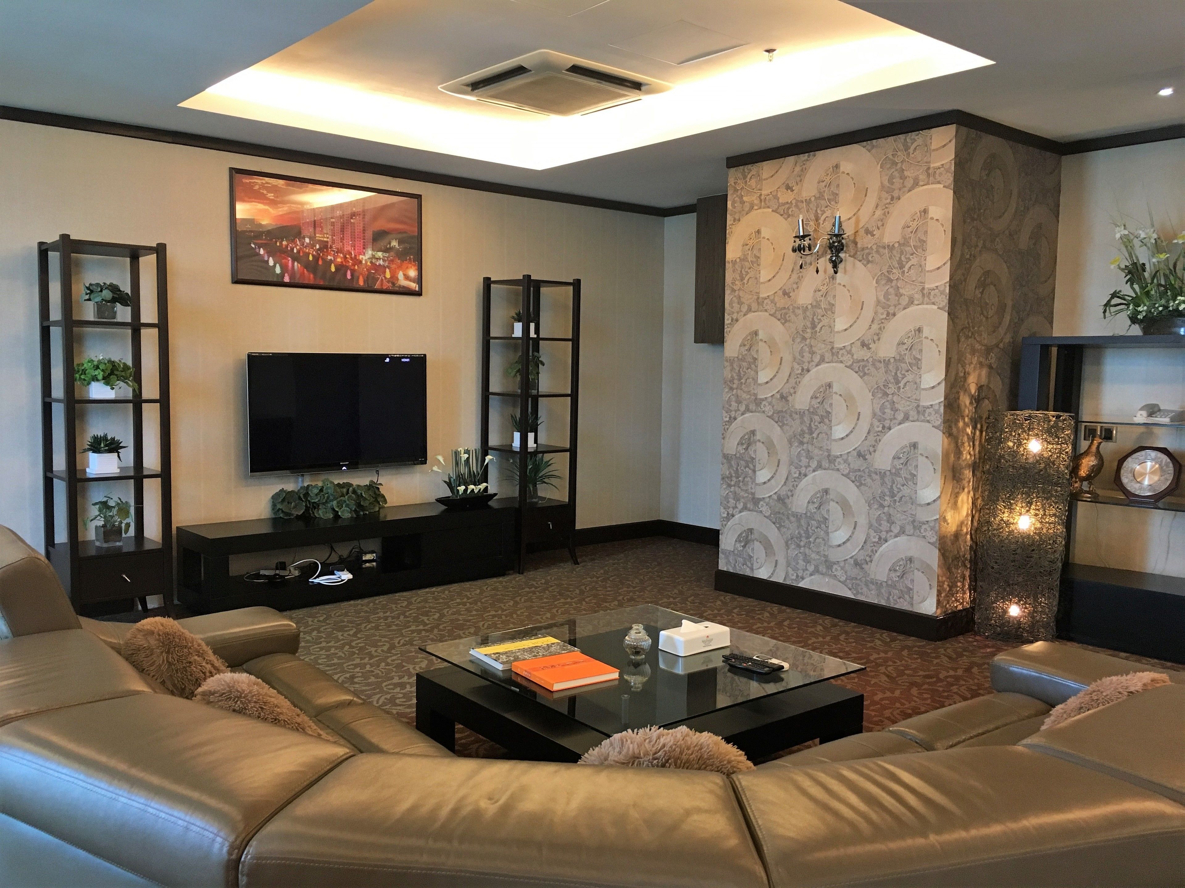 A modern living room with leather sofas, a flat-screen TV, and decorative shelves.