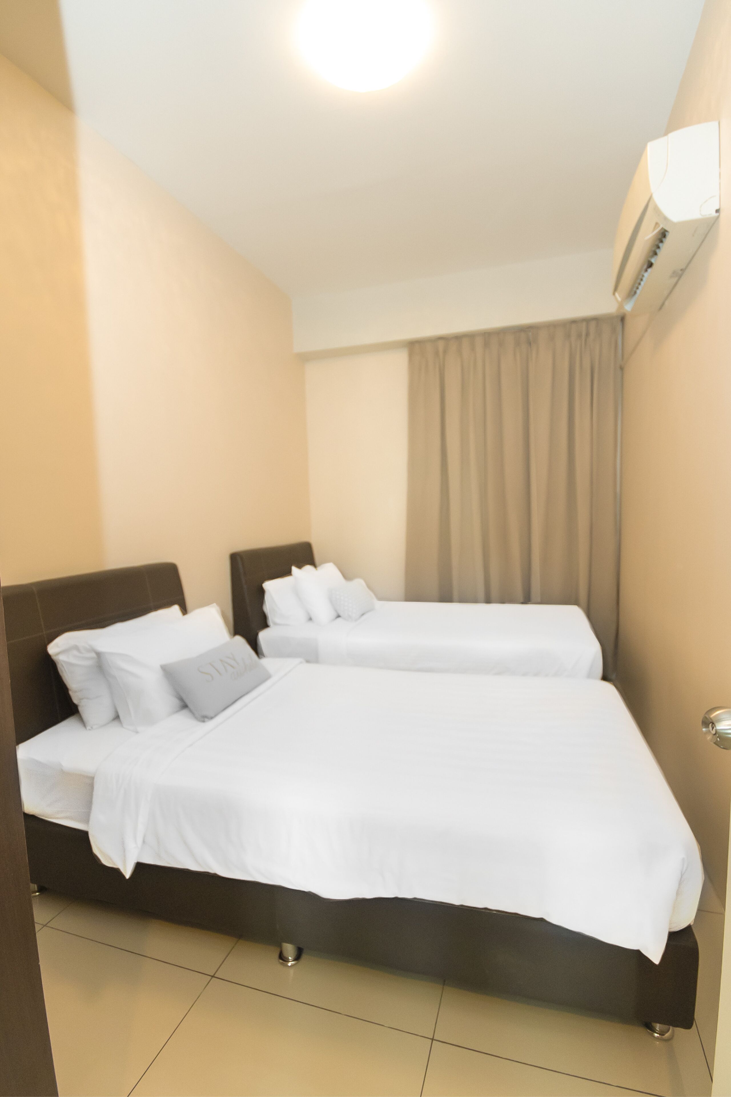 A hotel room with two beds, a ceiling light, an air conditioning unit, and a curtain.