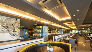 Un restaurante con una decoración moderna, que presenta un mural grande, zonas de estar con cabinas y mesas, y una barra con un menú a la vista.