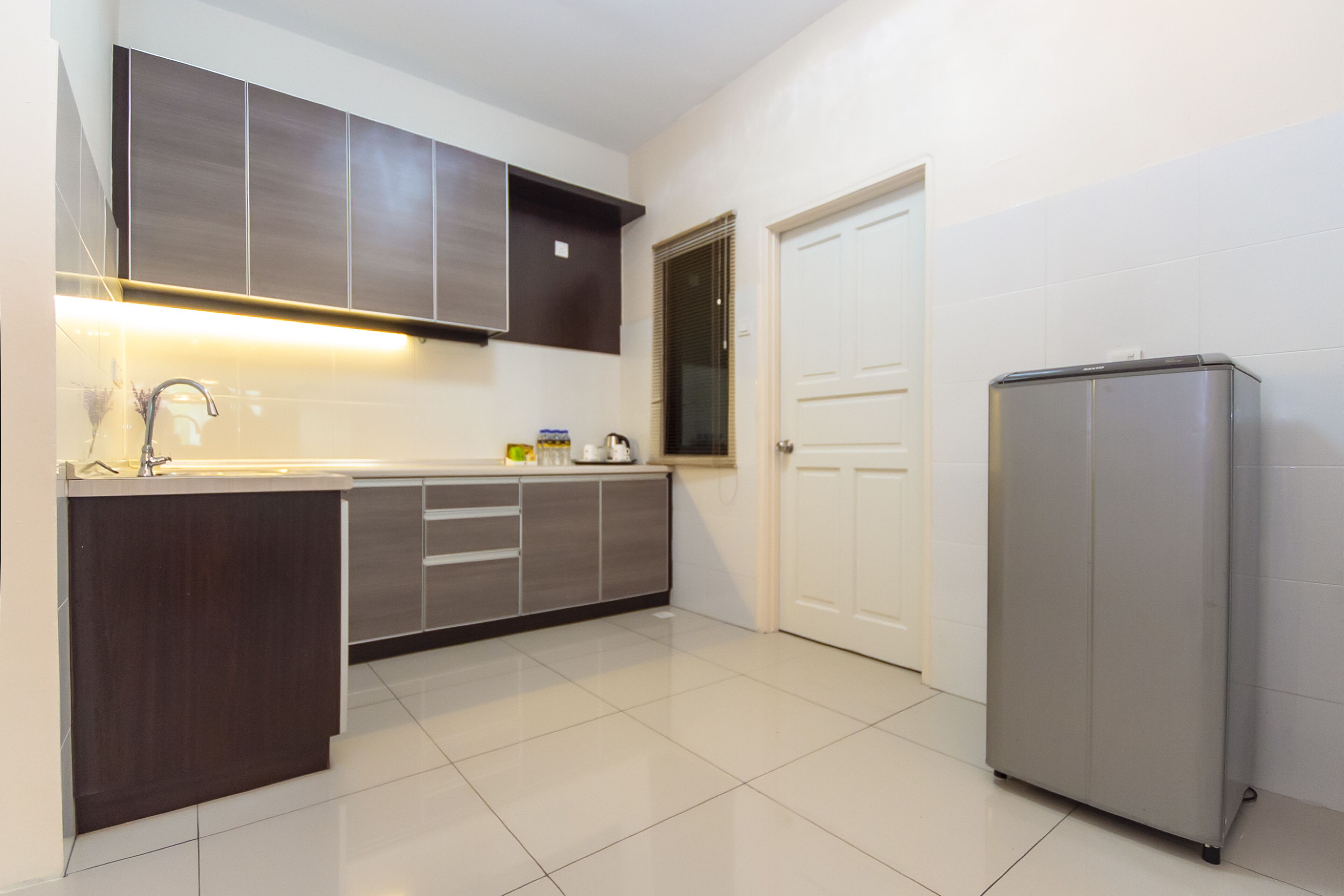 A modern kitchen with dark cabinets, a stainless steel refrigerator, and a white tiled floor.
