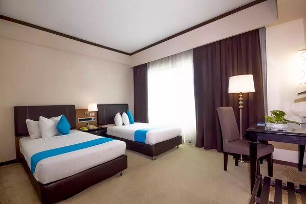 A hotel room with two beds, a desk, a chair, a lamp, and a window with curtains. - Kinta Riverfront Hotel & Suites (Ipoh)