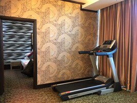 Une chambre d’hôtel équipée d’un tapis de course, d’un lit avec une tête de lit à motifs et d’un mur décoratif.