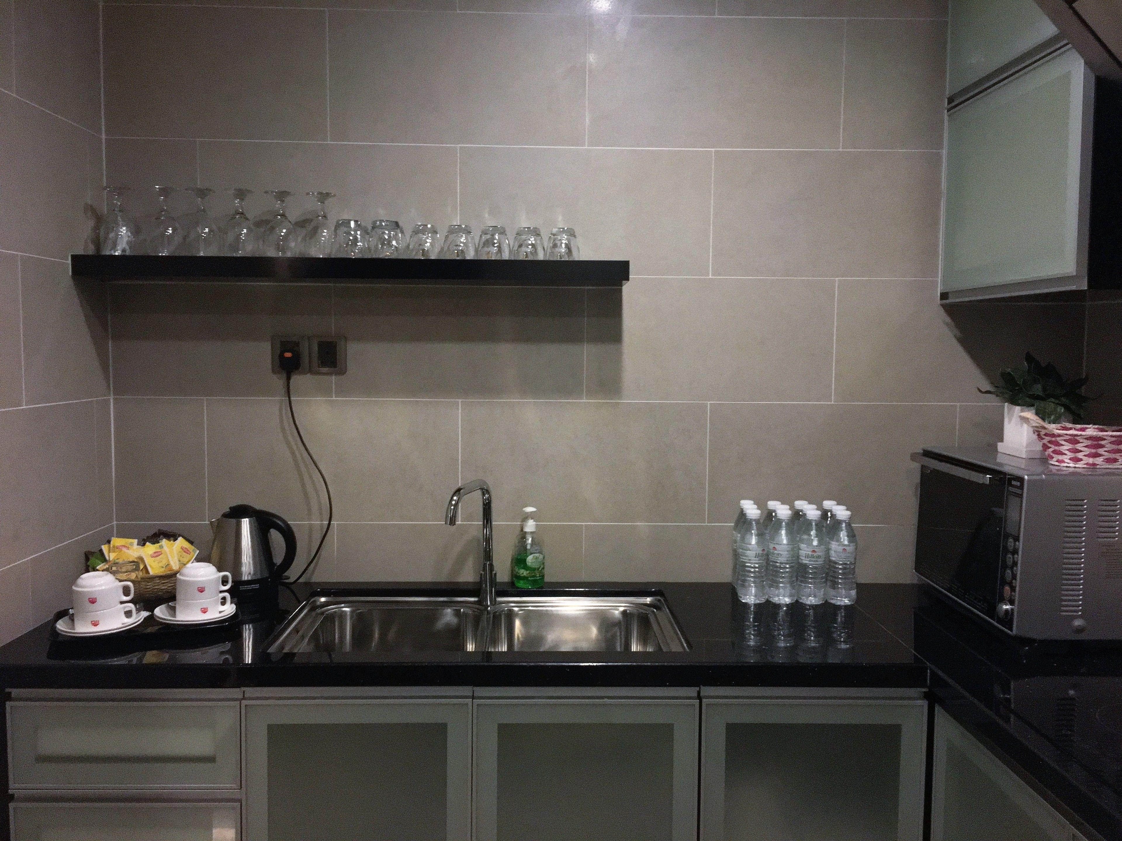 A kitchen with a stainless steel sink, a microwave, and a shelf with glassware.
