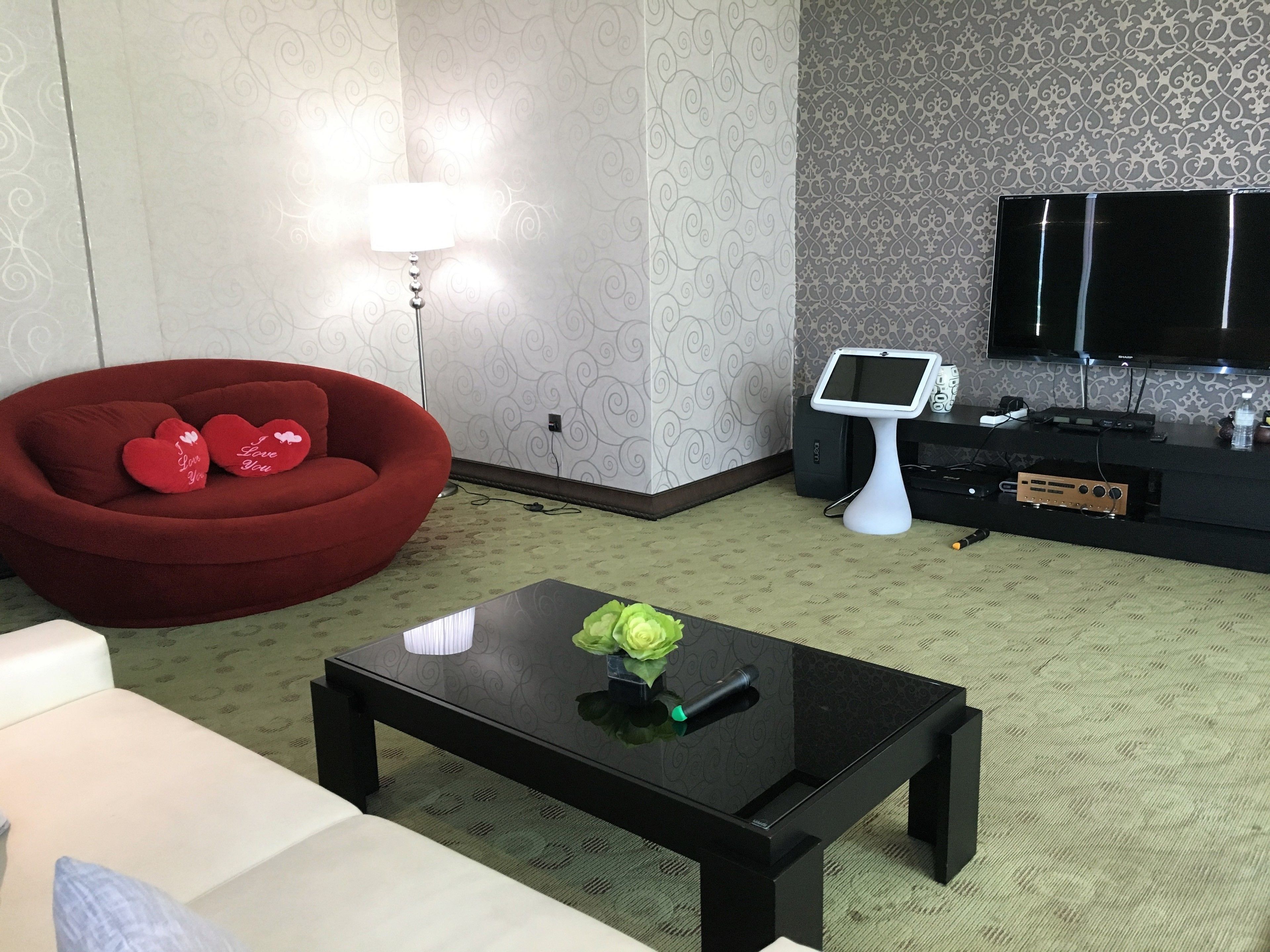 Una sala de estar moderna con un sofá rojo, una mesa de centro negra con un florero, un televisor de pantalla plana y un pequeño mostrador.