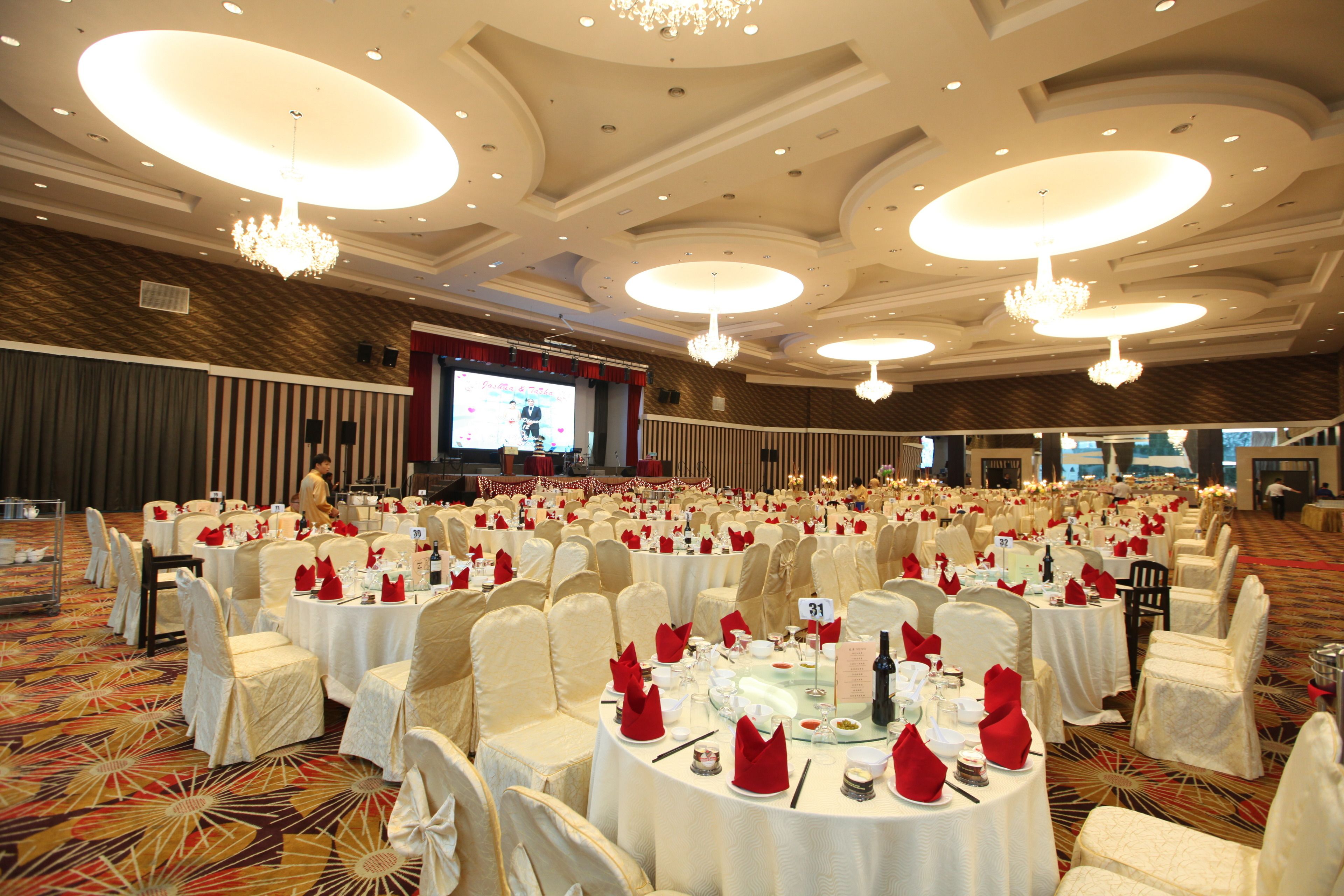 Un salón de banquetes con mesas redondas, sillas blancas y candelabros.