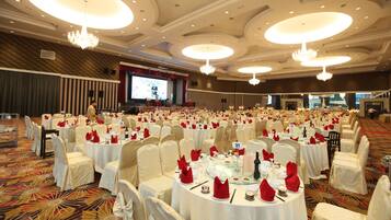 Un salón de banquetes con mesas redondas, sillas blancas y candelabros.