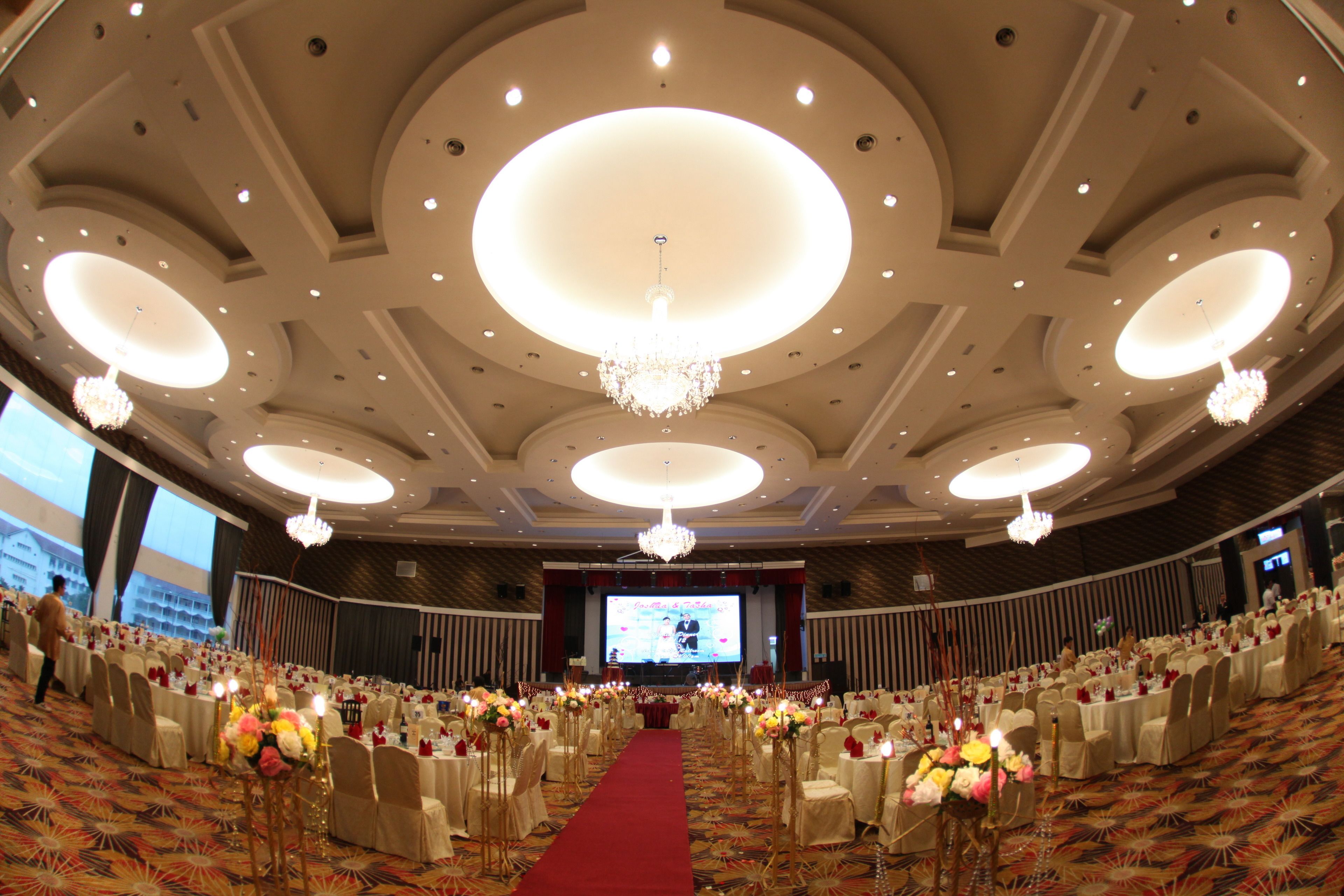 Un salón de banquetes con alfombra roja, mesas redondas y candelabros.