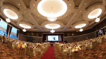 Un salón de banquetes con alfombra roja, mesas redondas y candelabros.