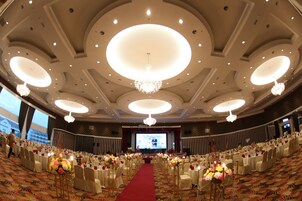 Un salón de banquetes con alfombra roja, mesas redondas y candelabros.
