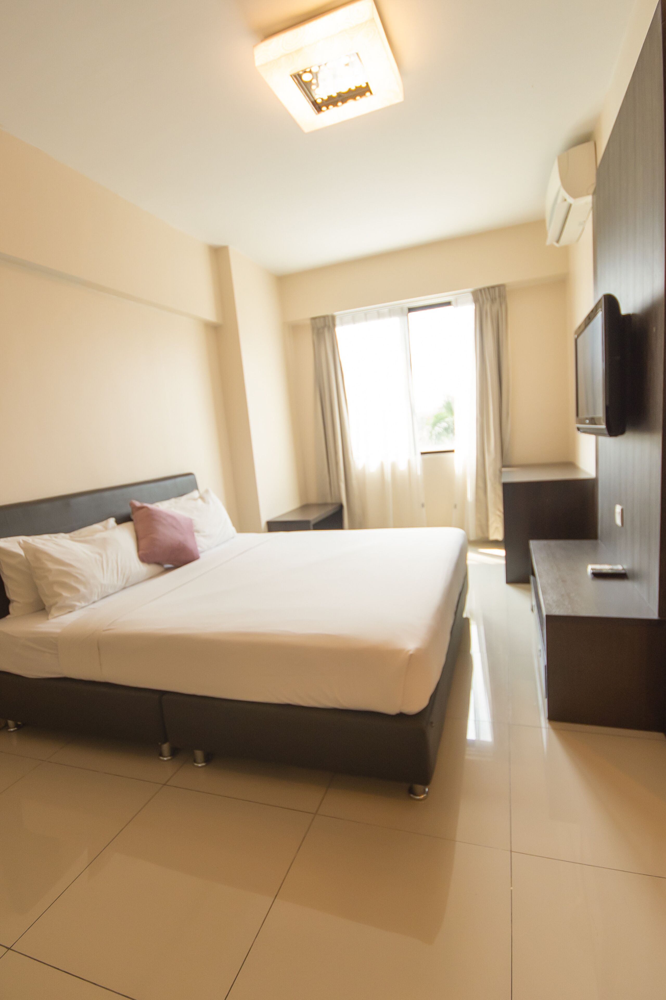 A hotel room with a large bed, a bedside table, a TV, and a window with curtains.