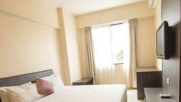 A hotel room with a large bed, a bedside table, a TV, and a window with curtains.