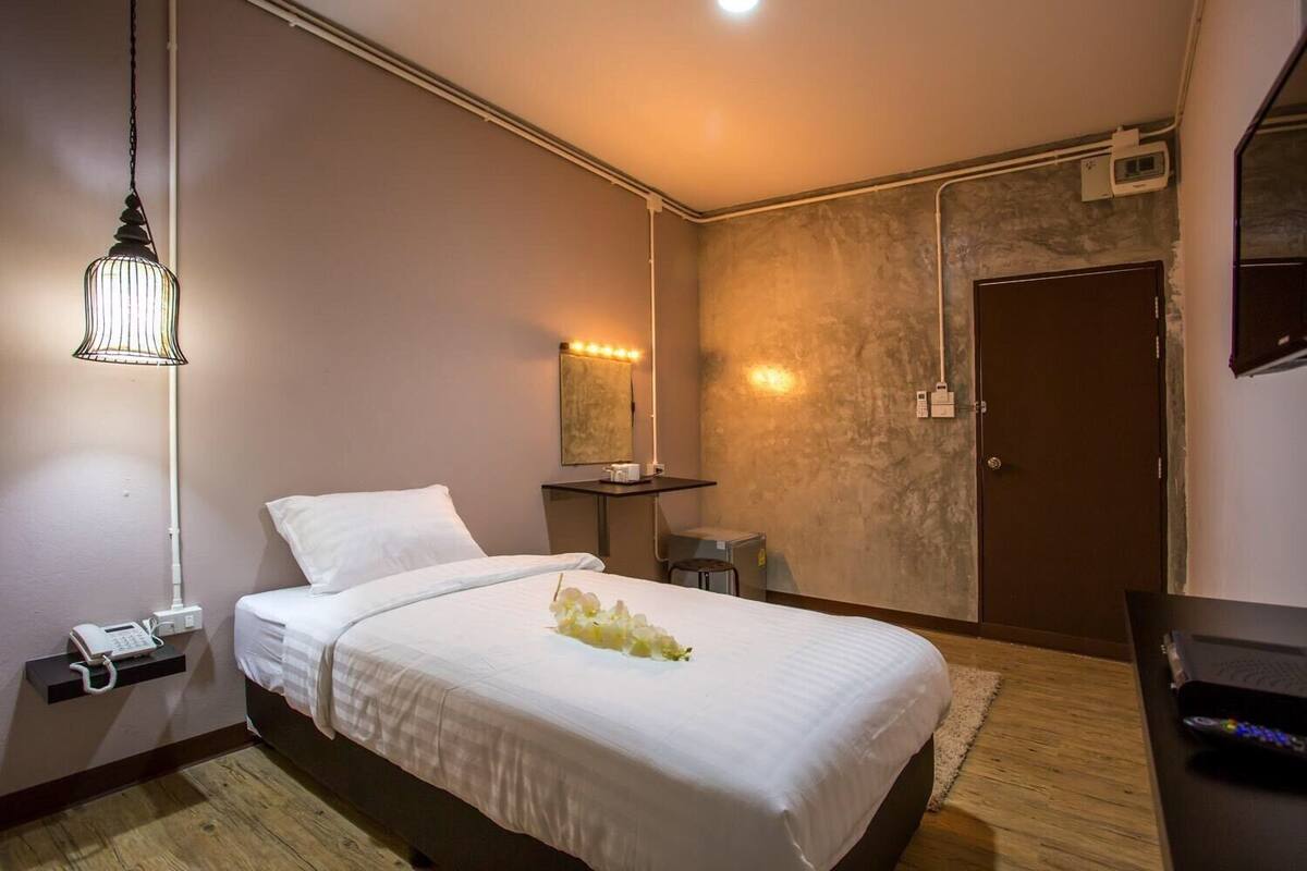 Ein Hotelzimmer mit Bett, Nachttischtelefon, Nachttischlampe, Nachttisch und Spiegel.