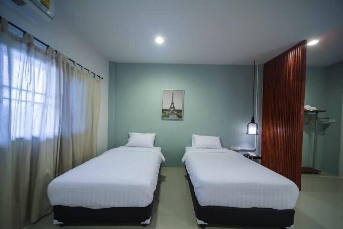 Ein Zimmer mit zwei Einzelbetten, einem Gemälde des Eiffelturms, einem Schreibtisch mit Lampe und einer Holzwand.