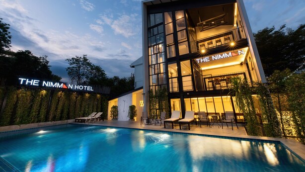 A modern hotel with a swimming pool, outdoor seating, and a well-lit facade. - The Nimman Hotel (Chiang Mai)