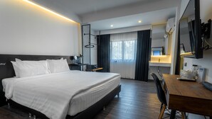A modern hotel room with a large bed, a wooden desk, a mirror, and a view of the city through the window. - The Nimman Hotel (Chiang Mai)