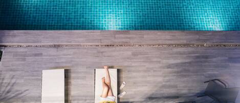A poolside area with two sun loungers and a chair, a tiled pool, and a stone wall.