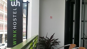 Een balkon met een bordes waarop 'Wink Hostel' staat, een bloempot en twee rieten stoelen.