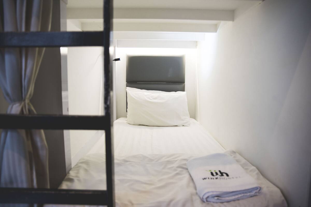 A narrow, dimly lit room with a bed, a pillow, and a folded towel.