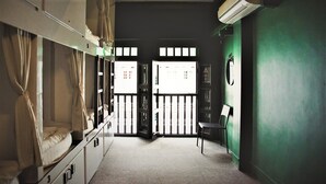 Een slaapzaal met stapelbedden, een stoel en een deur naar een balkon.