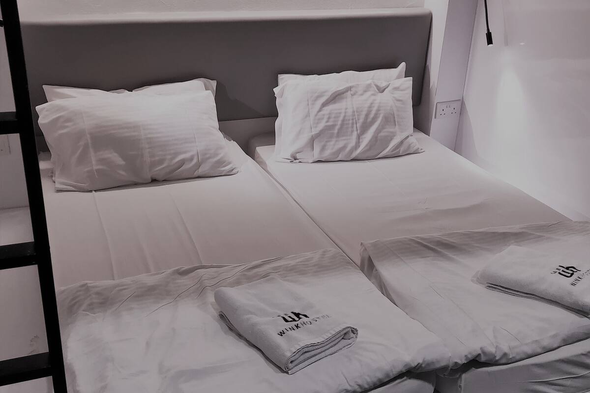 A single bed with white bedding and pillows, a headboard, and a power outlet on the wall.