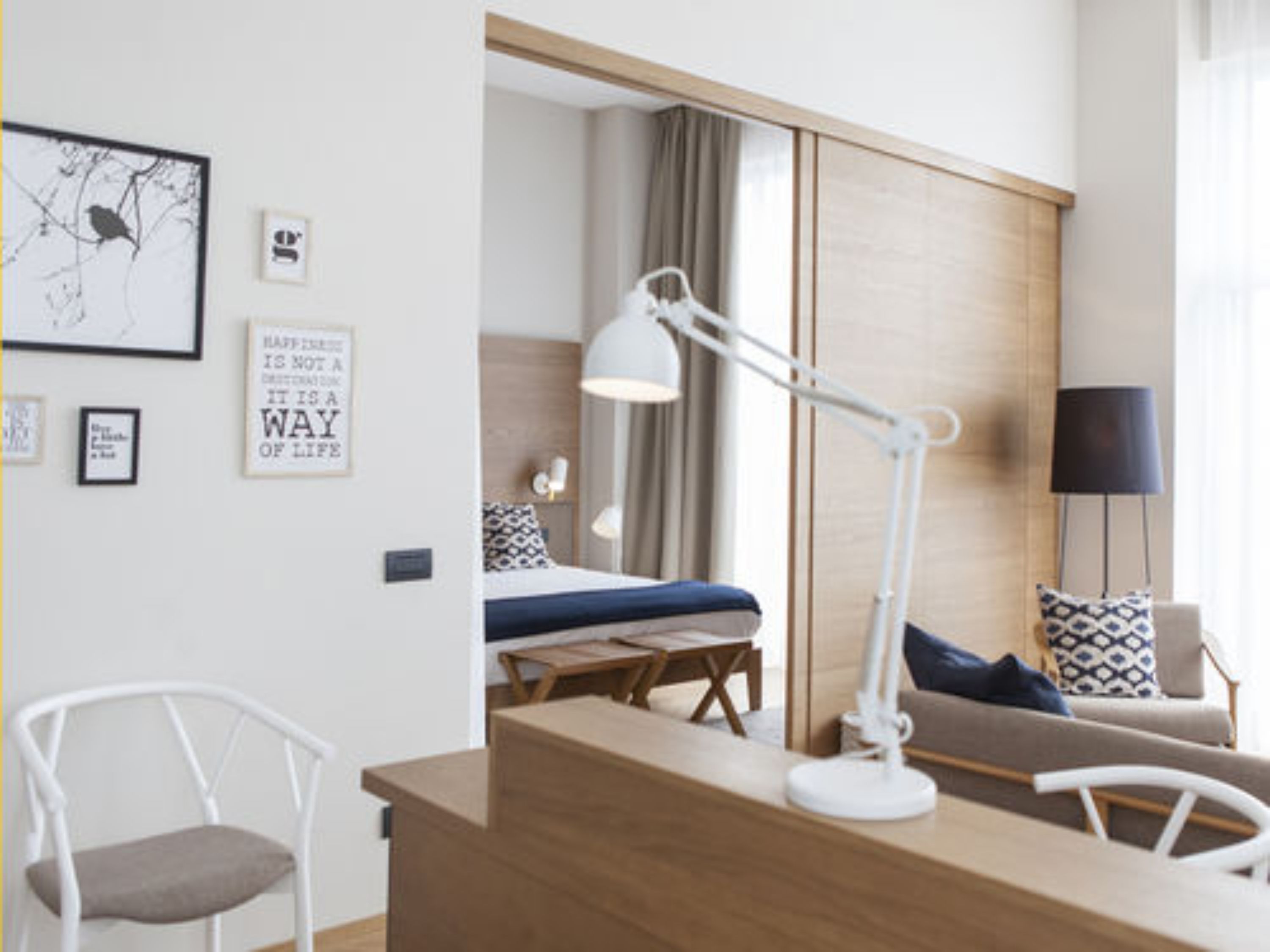 Ett modernt hotellrum med en säng, ett skrivbord, en stol och en lampa.