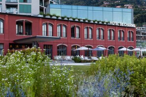 En rød bygning med skiltet "HOTEL DE CHARME" og udendørs siddepladser med parasoller.