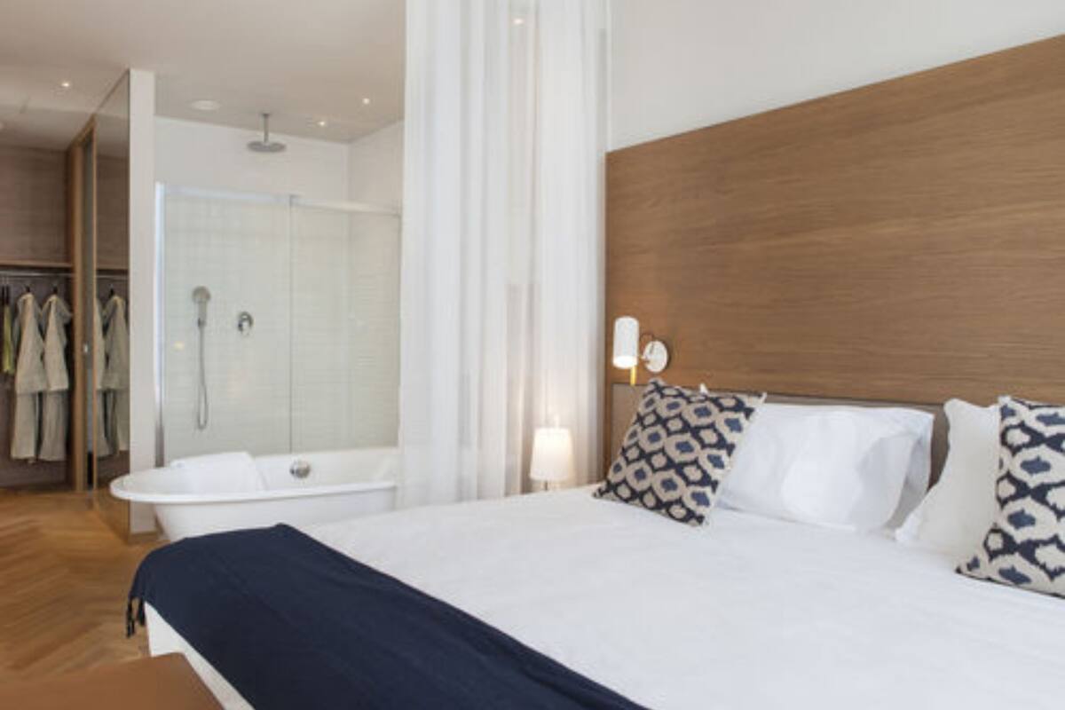 Une chambre d’hôtel moderne dotée d’un grand lit, d’une tête de lit en bois, d’un espace douche et d’un dressing.