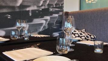Een eettafel gedekt met wijnglazen, borden en bestek, met een bank en gestreepte kussens op de achtergrond.