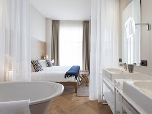 Et moderne hotelværelse med en stor seng, et siddeområde med en bænk, et stort badekar og et separat bruseområde.