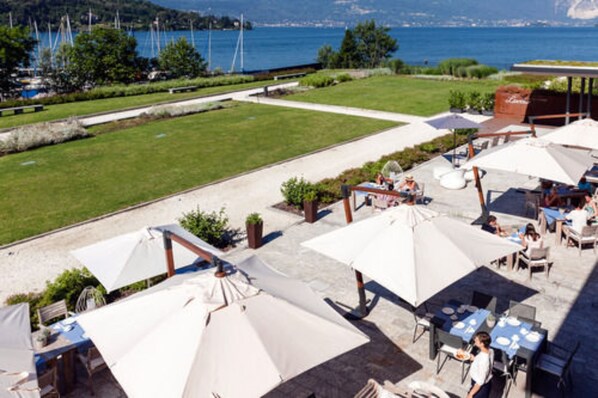 Une terrasse extérieure avec des tables et des parasols, offrant une vue sur un plan d’eau et des collines.