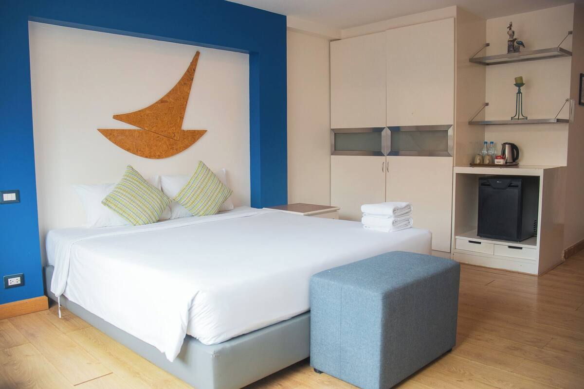A modern bedroom with a large bed, a blue accent wall, a wooden crescent moon decoration, and a built-in TV shelf.