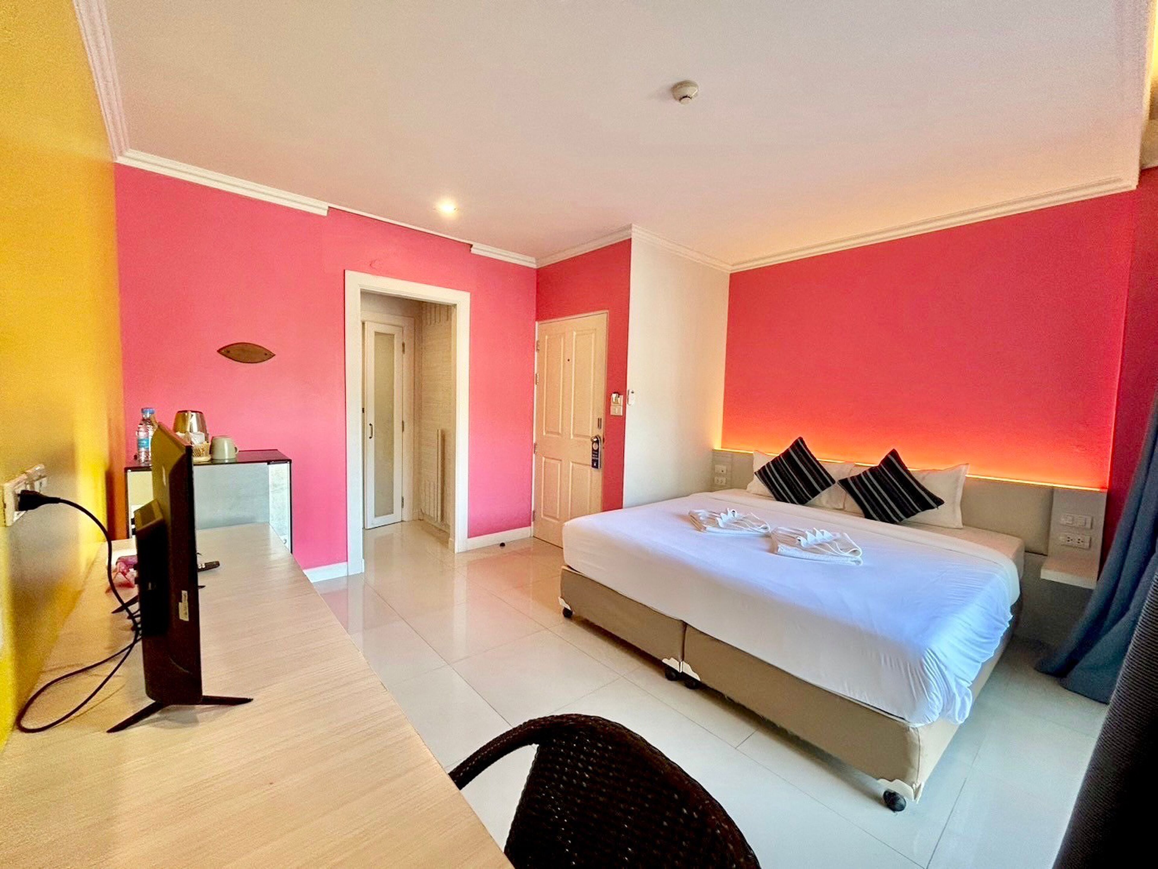 A hotel room with a large bed, a desk with a computer, and a bathroom visible through an open door.