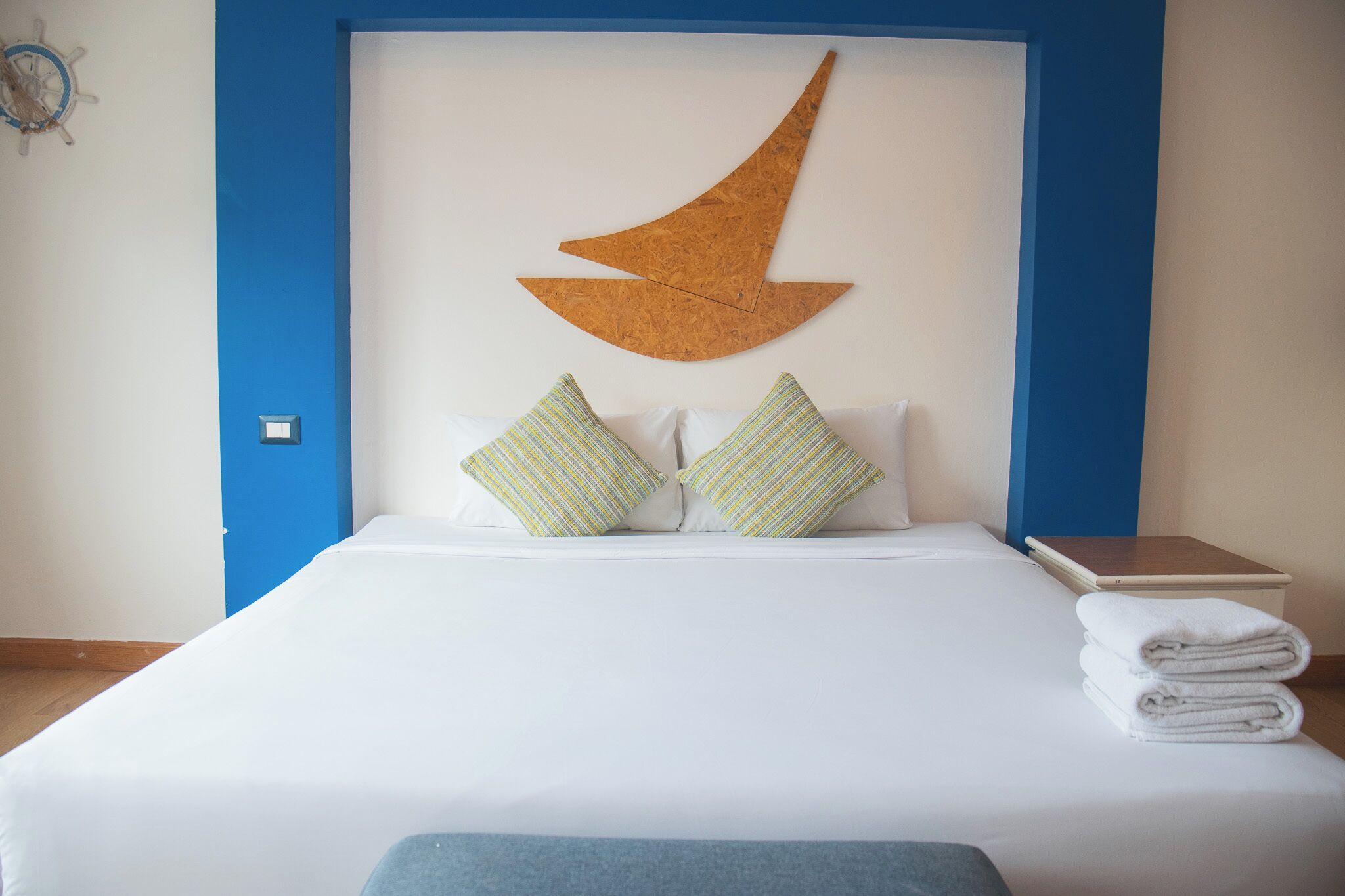 A neatly made bed with white linens, two striped pillows, and a wooden crescent moon decoration on the headboard.