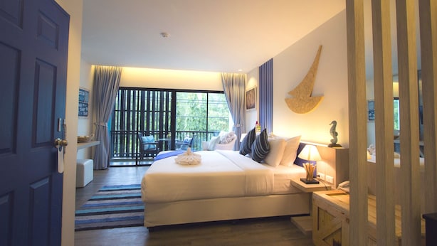 Un dormitorio con una cama grande, un escritorio con lámpara, una ventana con cortinas y vistas al exterior.