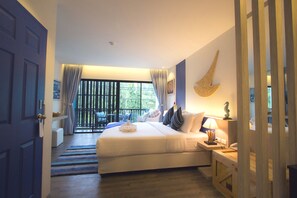 A bedroom with a large bed, a desk with a lamp, a window with curtains, and a view of the outdoors. - The Blue Pearl Kata Hotel (Karon)